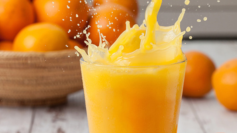 Orange juice splashing into a glass with some out of focus oranges in the background