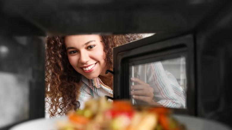 person reheating food in microwave