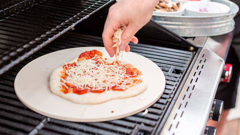 Person preparing pizza on stone on grill
