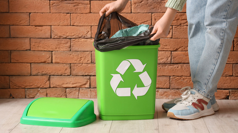 someone changing bag of green recycle bin