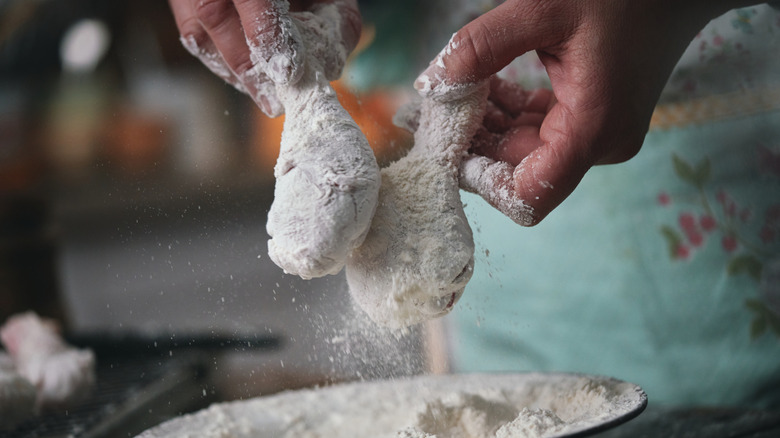person dredging chicken legs in flour