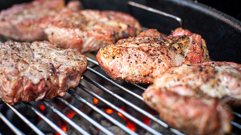 steaks sear over coals on a grill