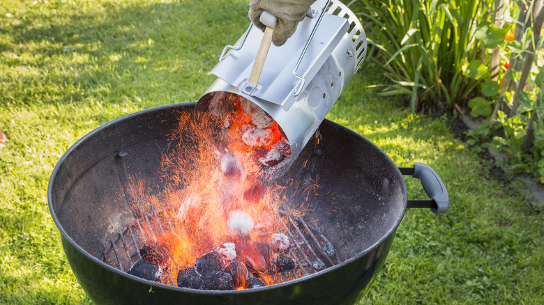 Hand adding layers of coal to a bbq from a chimney