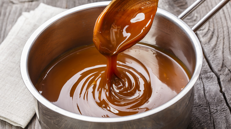 Liquid caramel in a steel pot with wooden spoon