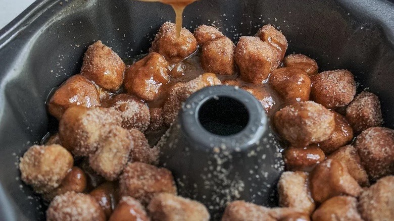 Sugar and cinnamon-coated dough balls being drizzled with melted butter in a Bundt pan