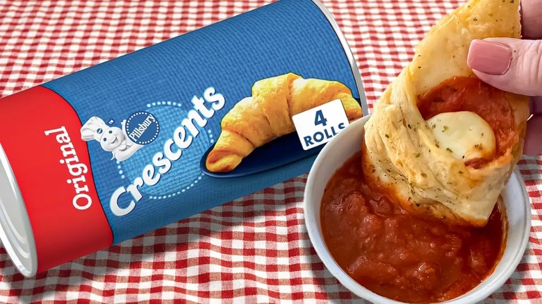 A package of crescent rolls with a mini pizza being dipped in marinara