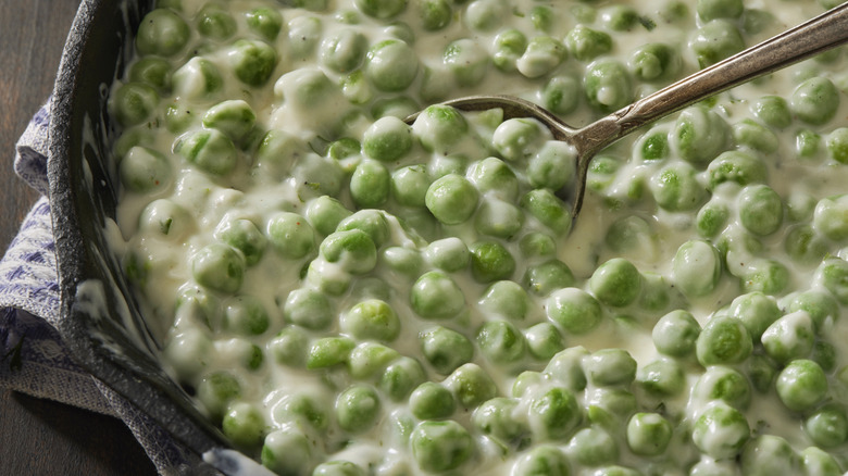 A bowl of creamed peas with a spoon resting in them.