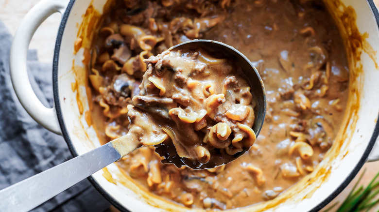Beef stroganoff with ground beef in a ladle over a large white pot with the same.