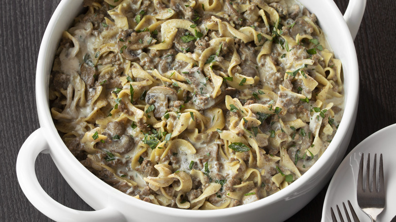 Beef stroganoff with egg noodles in a large white pot with handles.