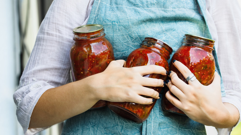 A person in a teal linen apron juggles three glass jars of tomato sauce