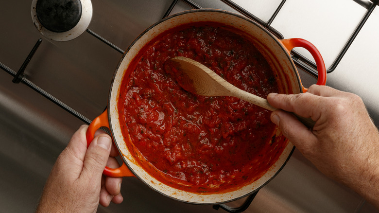 A person stirs a Le Creuset pot full of tomato sauce