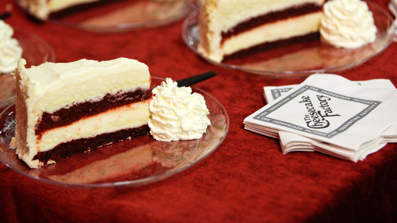 Slices of cheesecake beside a stack of Cheesecake Factory branded cocktail napkins