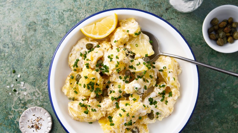 Creamy potato salad in a bowl with lemon wedge, chives, and capers