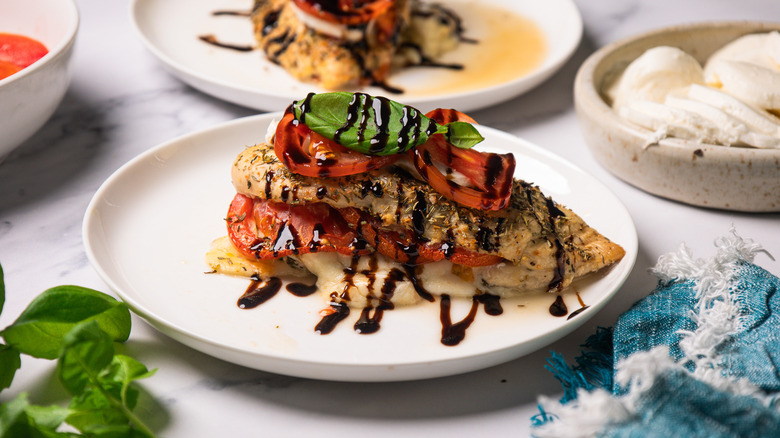 A Caprese-stuffed chicken breast on a white plate next to blue napkin
