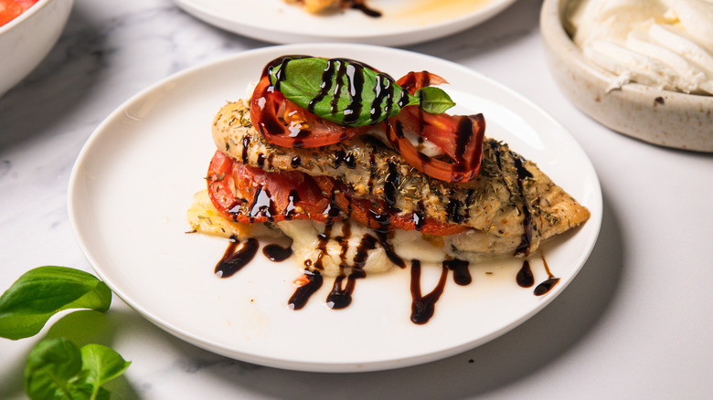 A Caprese-stuffed chicken breast on a white plate next to basil