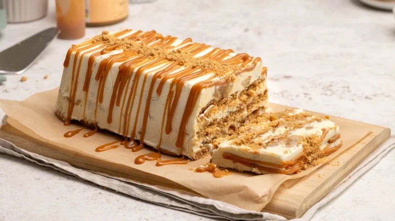A caramel apple icebox cake with a slice cut off the end sits on parchment paper on a countertop.