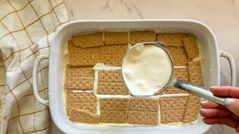 hand adding more pudding to graham cracker layer of cake