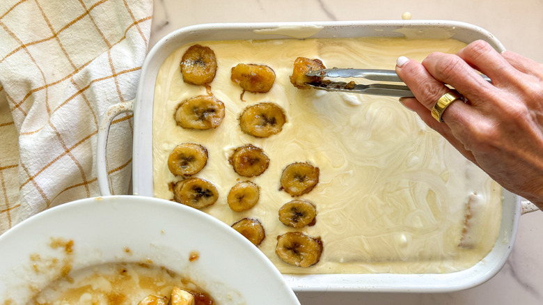 hand adding second layer of bananas to pudding in baking dish