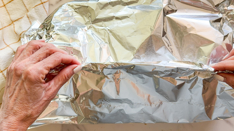 hand pinching foil on top of baking dish