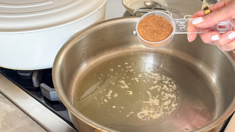 hand adding brown sugar to pan with melted butter