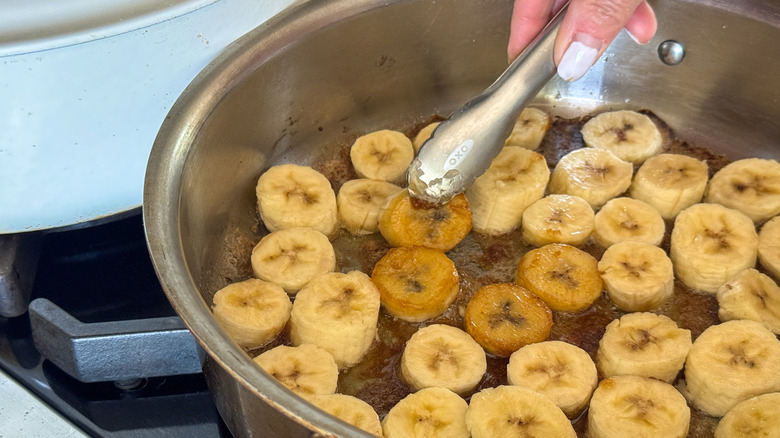 hand using tongs to flip banana slices in skillet