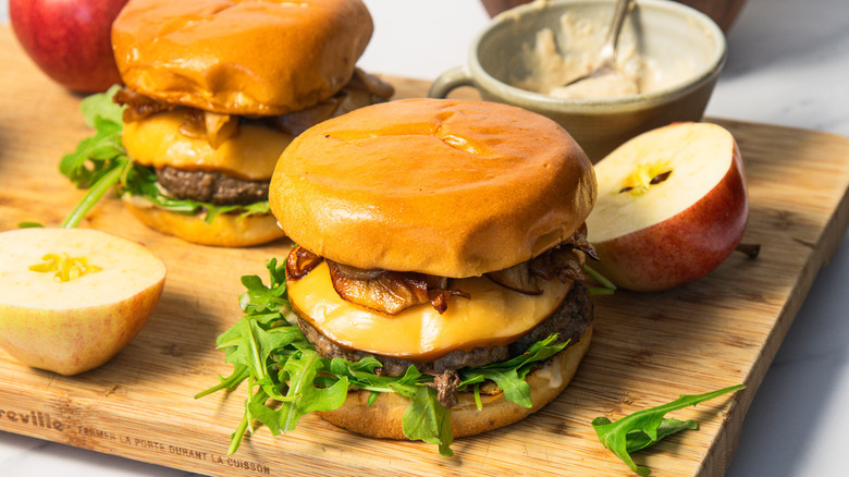 Two caramelized apple burgers on a cutting board with apples
