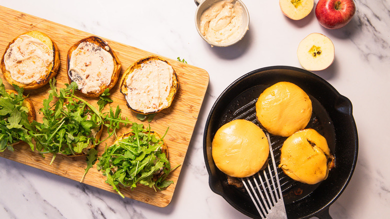Caramelized apple burgers on a cutting board with buns being smeared