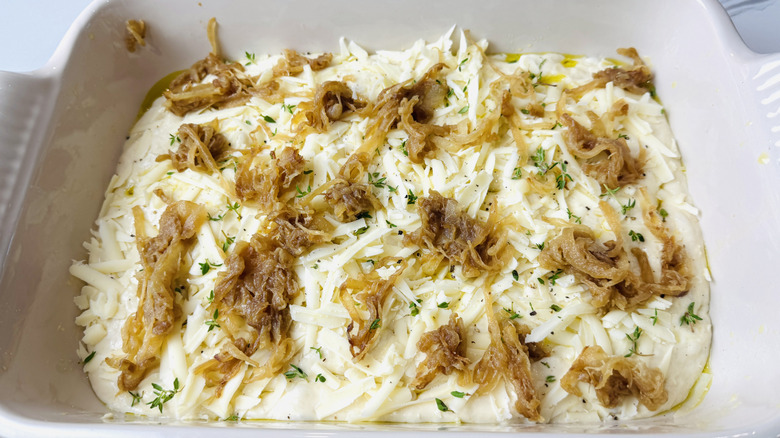Focaccia dough topped with shredded cheese, thyme, and caramelized onions