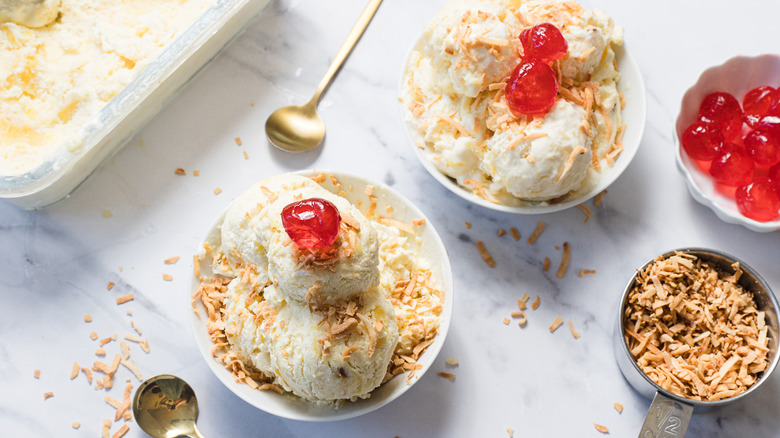 Two pineapple ice creams with maraschino cherries and spoons