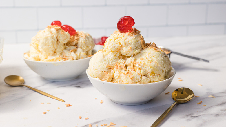 Two pineapple ice creams with maraschino cherries and spoons