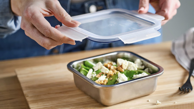 Hands putting a lid onto a stainless steel food storage container.