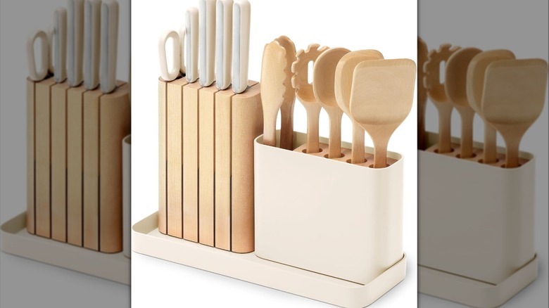 Sleek wooden knife block and cream-colored utensil holder on a tray with various knives and utensils.