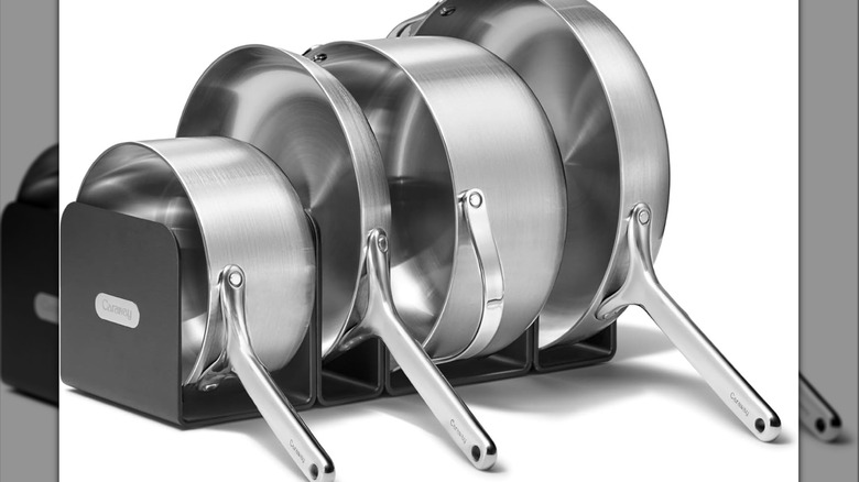 Four different sized stainless steel pots and pans on a black organizing rack.