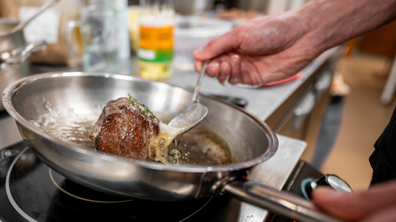 Basting a steak with butter in a stainless steel pan.