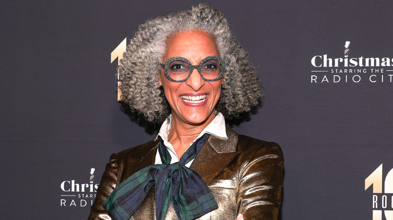 Carla Hall with glasses and blazer with scarf tied into bow