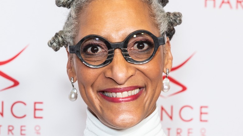 Carla Hall smiles with red lips and round glasses