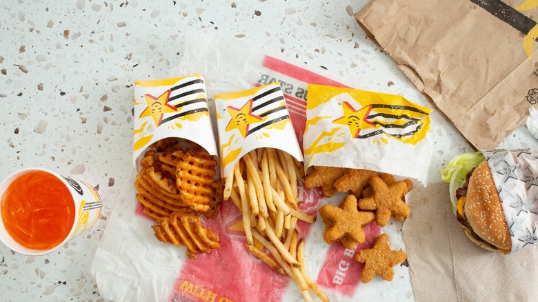 an orange drink, waffle fries, fries, chicken stars and a burger from Carl's jr