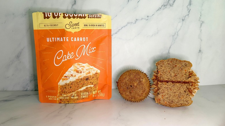 Sweet Logic Ultimate Carrot Cake Mix package next to two carrot cake cupcakes on marble surface