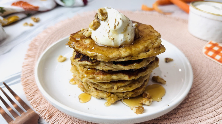 Carrot cake pancake stack on plate topped with cream cheese, syrup, and walnuts