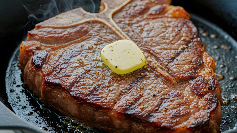 a t-bone steak with a pat of butter cooking in a cast iron skillet