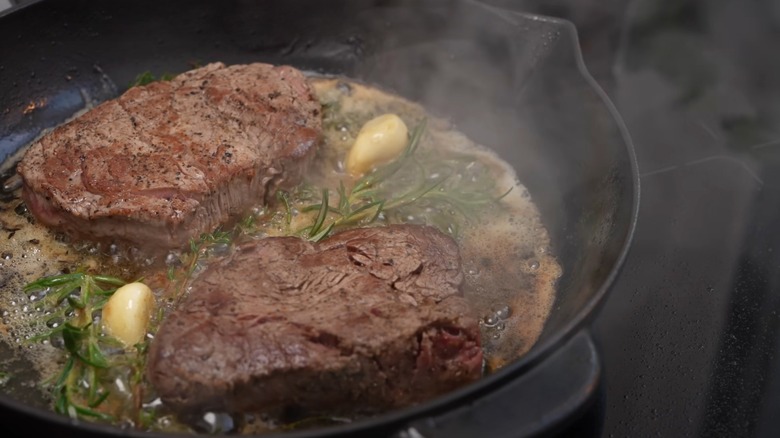 two steaks in a cast iron pan with butter and rosemary