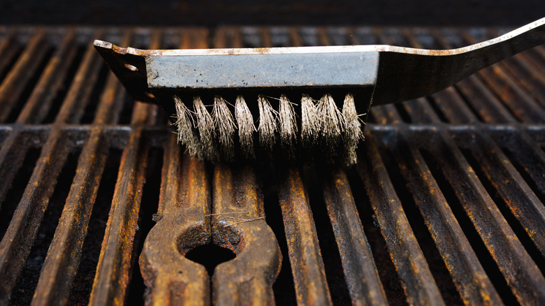 A close-up of a rusty cast-iron grill with metal brush