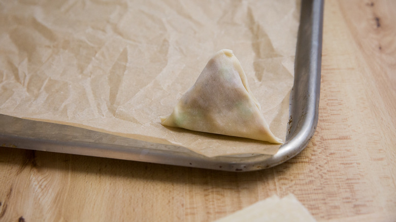 one uncooked samosa on pan