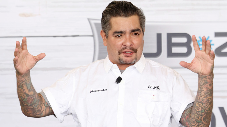 celebrity chef Aarón Sánchez in white chef's jacket holding up his tattooed arms