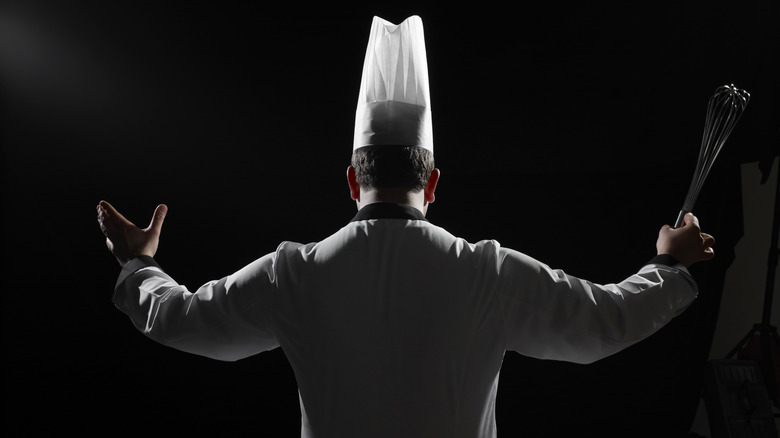 Chef in hat holding whisk with black background