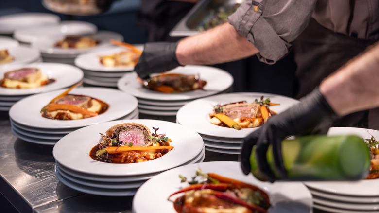 A close-up of a team of chefs in black gloves preparing multiples of dishes