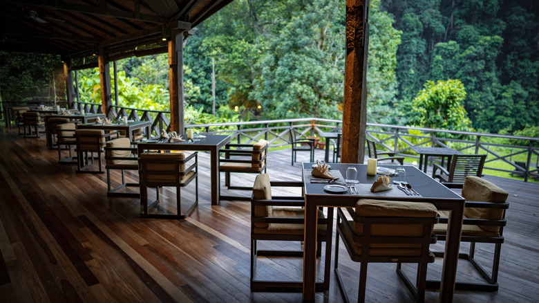 A minimalist restaurant dining area on a deck with wooden furniture overlooking a forest