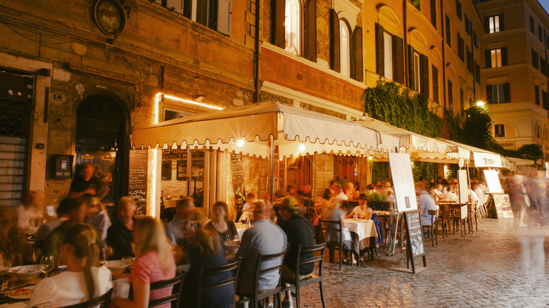 Crowded tables in front of an Italian restaurant with an awning at night