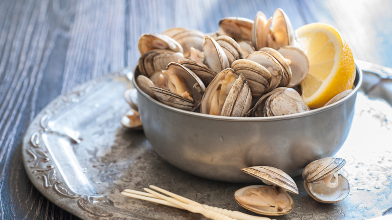 Bowl of cherry stone clams with a lemon half on a gray platter