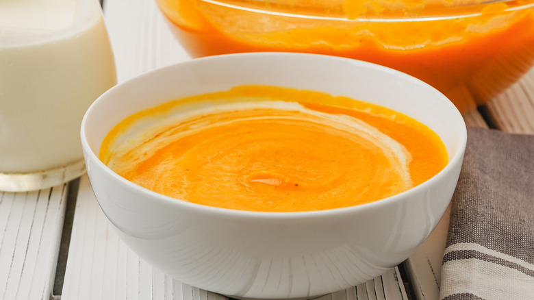 Bowl of butternut squash soup on a white table with more soup in the back
